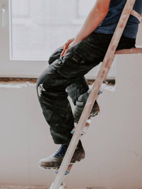 Mavi tişörtlü işten yorgun genç beyaz bir adam pencerenin arka planında kirli bir merdiven üzerinde oturur ve dinlenir, yakından bakar. Konsept duvar sıva, sıva hizmetleri