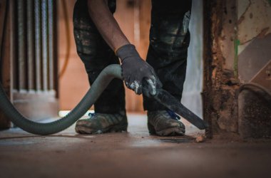 Üniformalı ve eldivenli tanınmayan genç bir beyaz adam inşaat süpürgesiyle etrafı süpürüyor. Yıkık duvarlı bir evin ana kirli geçidi. Tamirat için hazırlanıyor.