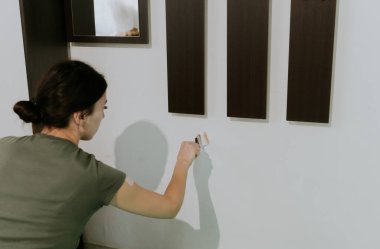 Genç, güzel bir Kafkas esmer, çömelmiş, dış görünüş için gardırobun altından fırçayla duvarı beyaz boyayla boyuyor..