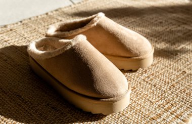 Bir çift modern modaya uygun, sıcak Uggs terlikleri yüksek bir platformun ortasında, bir kış günü fayanslı zeminde örülmüş jüt bir halının üzerinde, güneşten gelen gölgeler ve yakın bir yan görüş ile uzanıyor. Modaya uygun.