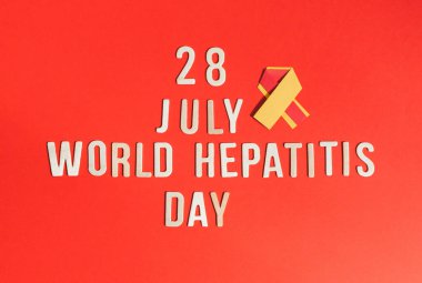 Üzerinde ahşap sayılar ve harfler olan sarı-kırmızı bir kurdele. 28 Temmuz hepatit günü kırmızı arka planda yatar..