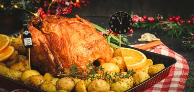 Patatesli tavuk, otlar, portakal ve kağıt saat gece yarısı fırın kabında bir şişe şampanya ve siyah arka planda yeni yıl süslemesi..