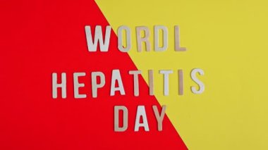Üzerinde Dünya Hepatit Günü yazan hafif ahşap harfler kırmızı ve sarı bir arkaplanda, düz bir zeminde, zoom out ile yakın çekim, yavaş çekim şeklinde uzanır. Dünya Hepatit Günü konsepti.