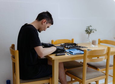 Siyah lateks eldivenli yakışıklı beyaz bir adam laptopun kapağını kapatır. Tozdan temizler ve onarır. Bir yaz günü mutfaktaki masada oturur.