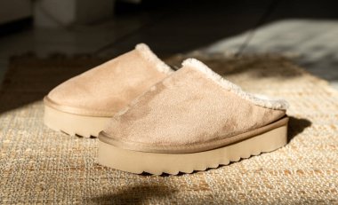 Bir çift modern modaya uygun, sıcak Uggs terlikleri yüksek bir platformun ortasında uzanır. Örülmüş bir halının üzerinde. Bir kış günü oturma odasının fayanslı zemininde.