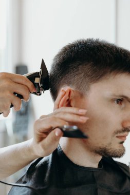 Tanınmayan genç bir kadın kuaförün elleri sağ şakak bölgesinin saçını kesiyor, parmağını kulağına bir saç makasıyla tutuyor ve bir yaz günü evde esmer bir adama uzanıyor.