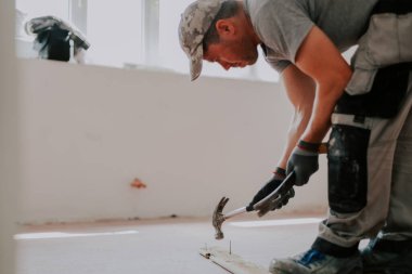 Üniformalı ve tekstil gri eldivenli yakışıklı beyaz adam sökülmüş eski bir ahşap kadifeden çivi ve levyeyle çivi çıkarıyor.