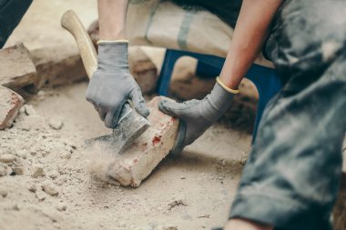 Siyah iş elbiseli beyaz bir genç adam sağdaki küçük bir sandalyeye oturur ve toprak, enkaz ve eski çimentoyu balta ile temizler. İnşaat konsepti..