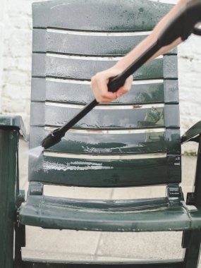 Gri eşofmanlı ve tişörtlü beyaz bir adam evinin arka bahçesindeki koyu yeşil güneş musluğunun altında plastiği yıkıyor. Güneş ışığı, ev yıkama konsepti.
