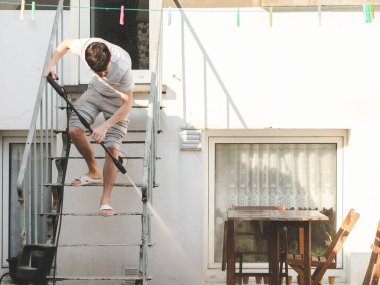 Gri spor giyen beyaz bir adam ve arkadan gelen bir tişört bir Karcher metalinin basıncıyla yıkanır evinin arka bahçesindeki teraslara kadar merdiven, yan görüş, yakın çekim. Şey...