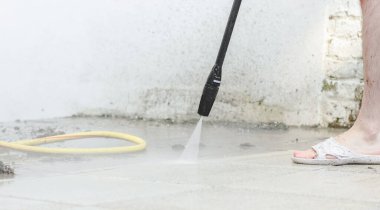 Genç beyaz bir adam evinin arka bahçesindeki duvarın yakınındaki bir Karcher 'la güçlü su basıncıyla kirli fayansları yıkıyor. Bahçe temizliği, ev temizliği kavramı