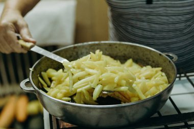 Tanınmayan yaşlı beyaz bir kadın, bir yaz günü, bir kır evinde, yakın çekim manzarası olan bir ocakta tavada kızarırken metal spatula kullanarak kızarmış patates fırlatıyor. Konsept