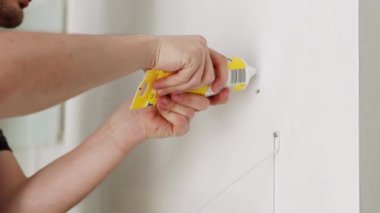 Genç bir beyaz adam macunu tüpten çıkarır ve bir bahar günü beyaz bir duvardaki vida deliğini kapatır. Saha derinliği ve yavaş çekim gücüyle yakın çekim yan görüntüsü..