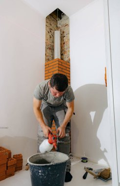 Kafkasyalı genç bir adam, odasındaki şöminenin duvarcılık bacası için basınçlı sprey şişesinden çıkan suyla bir kovada çimento havanı ıslatıyor. Temiz tuğla işi