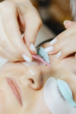 Beyaz önlüklü beyaz bir kozmetik uzmanı genç bir kızın portresi silikon bir kalıba pembe plastik fırça kullanarak kirpiklerini yapıştırıyor kozmetoloji masasında yatan esmer bir kadına.