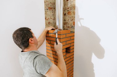 Taze çimento harcı döşeyen genç beyaz bir adam, çekiçle tuğlaya vuruyor, şöminenin bacasında temiz bir tuğla yapıyor, yan görünüş seçici bir odak ile kapanıyor. Temiz