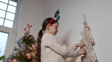 Saçında yeşil geyik boynuzları olan güzel bir beyaz kız duvardaki takvimin cebinden sürpriz bir hediye çıkarır ve sevinçle bir arka planda dikildiğini gösterir.