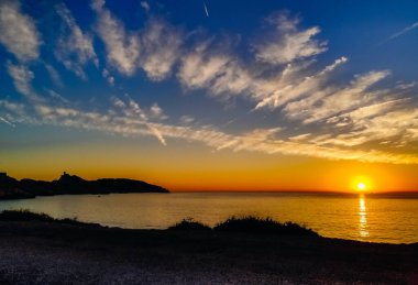 Fransa 'nın Marsilya kentindeki Frioul adasında, denizin ufukta görünen sarı günbatımı kumsalındaki batan güneşin güzel manzarası. Güzel kavram