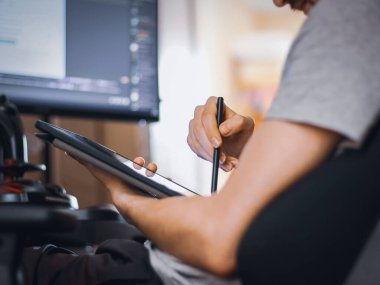 Gri tişörtlü yakışıklı beyaz bir adam çalışma koltuğunda oturuyor ve önünde beyaz ekran ve siyah kalemle bir tablet tutuyor. Evde bulanık bir şekilde yemek siparişi vermek için bir menü seçiyor.