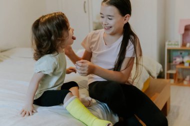 Yüzünde mutlu bir gülümseme olan iki güzel beyaz kız, etrafta dolanıyor, dilini gösteriyor, sabahın erken saatlerinde yatakta oturuyor, derinlik ve derinlik ile yakından bakıyor.