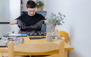 Siyah lateks eldiven giyen yakışıklı beyaz bir adam, bir yaz günü mutfaktaki masada otururken bilgisayarı tamir etmek için vantilatörlerin bağlantısını kesiyor. Bilgisayar onarımı