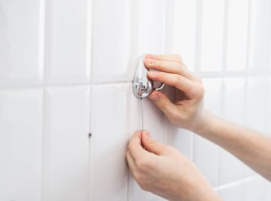 Genç beyaz bir adam banyoda eski metal bir havlu askısının vidalarını söküyor. Kıvrımlı küçük bir tornavidayla..