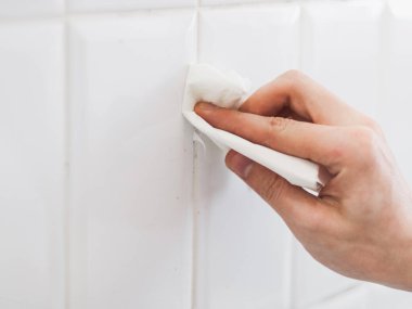 Tanınmayan genç bir beyaz adam, bir eli silikonlu bir silikonla banyoda fayanslı bir duvarda kağıt havluyla tuvalet temizliyor..