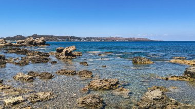Güneşli bir yaz gününde, Yunanistan 'ın Rodos adasının uzak bir köşesinde açık deniz ve kıyı kasabası olan ıssız kayalık bir plajın güzel manzarası.
