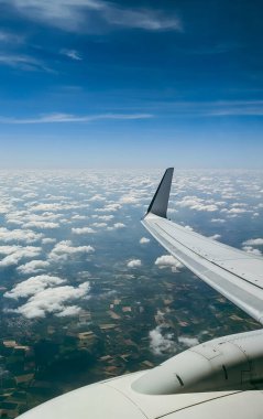 Tarlaların güzel hava manzarası, kırsal bölgelerdeki yerleşim yerleri ve uçuş sırasında uçağın penceresinden çıkan beyaz bulutların arasından geçen motorlu bir kanadın bir kısmı, yakın çekim yan görüntüsü.