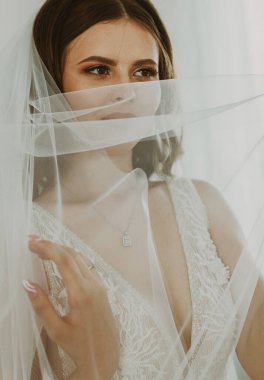 Beyaz elbiseli, beyaz elbiseli, güzel, beyaz tenli bir gelinin portresi yüzünü peçeyle örtüyor ve yan, alt, yakın çekim..