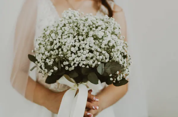 stock image Portrait of one unrecognizable young Caucasian bride in a white dress and veil holding a wedding bouquet of white boutonnieres in her hands in front of her, side view, close-up.