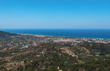 Beautiful panoramic view of a modern settlement near the coastline of the Aegean Sea in a mountainous area in Greece on the island of Rhodes on a summer sunny day, side view from Mount Filerimos close up. clipart