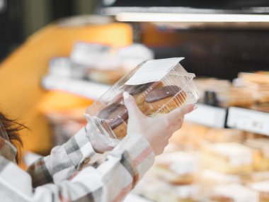 Ekose gömlekli genç beyaz bir kız tezgahın önünde dikilirken elinde bir kutu donut tutuyordu..