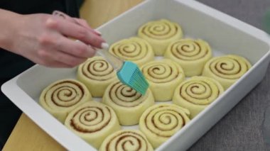 Genç bir Kafkas kızı yumurta sarısını şeker ve tarçınlı hamur parçalarının üzerine fırçalar, ahşap bir masada dikilir, yakından bakar. Cinnabon tarifi