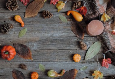 Sonbahar yaprakları, çam kozalakları, balkabakları, bir mum ve ortasında fotokopi alanı olan eski ahşap bir masa üzerinde yuvarlak bir çerçevede duran bir çelenk ve bir eşarp güzel bir görünüm
