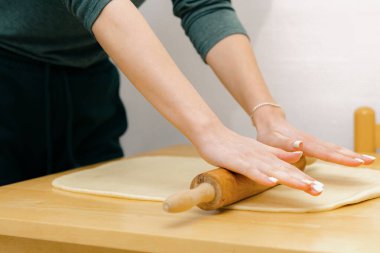 Tanınmayan genç beyaz bir kız hamur mayasını ince bir tabaka içinde ahşap bir masa üzerinde merdaneyle yuvarlıyor, mutfakta duruyor, yakından bakıyor. Pişirme için adım adım talimatlar