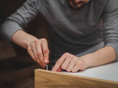 Kafkasyalı genç adam, yatağın altındaki çekmecenin parçalarını birleştiren bir anahtar ile vidayı sıkıyor, odasında yerde oturuyor, tarlanın derinliği ile yakın plan görüşü var. Birleştirme kavramı