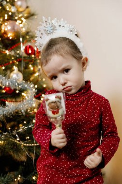 Beyaz kar taneleri tacı takmış küçük beyaz bir kız bir Noel ağacı ile gelişmekte olan takvimin arasında duruyor. Bir eliyle çikolatalı Noel Baba 'yı tutuyor ve bir gözünü kapıyor.