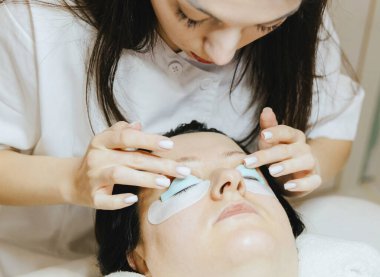 Beyaz önlüklü esmer kozmetik uzmanı genç bir kızın portresi parmaklarıyla silikon bir küf tutuyor ve bir kadının üzerinde yattığını inceliyor.