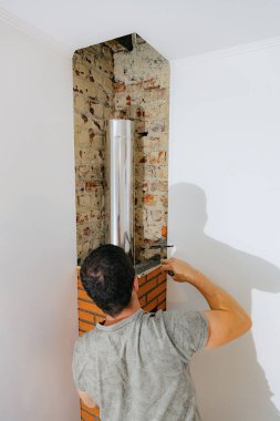 Genç beyaz bir adam arka tarafta duruyor ve spatula ve ince ahşap bir katman kullanarak taze çimento harcı düzleştiriyor. Odadaki şöminenin bacasında temiz bir tuğla yapıyor, yakın plan.