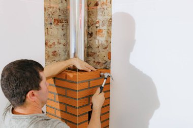 Genç beyaz bir adam çekiçle tuğlaya vurur, odadaki şöminenin bacasını lazer seviyesinde hizalar, seçici bir odak ile yan görüş sağlar. Temiz tuğla işi konsepti, ev