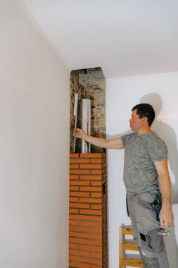 Genç yakışıklı beyaz bir adam lazer seviyesi ve cetvel seviyesini kullanır. Şöminenin bacasındaki tuğlaya yerleştirir. Seviyeyi kontrol eder, gündüzleri bir sandalyede durur ve kapatır.