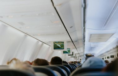 View of an electronic board with a flight path, inside a flying airplane with unrecognizable people sitting with their backs in chairs, close-up side view.