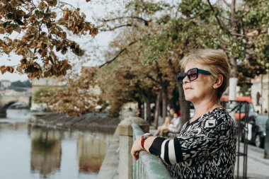 Güneş gözlüklü güzel, beyaz bir kadının portresi. Yalnız başına nehrin güzelliğine bakıyor. Prag şehrinde bir yaz gününde metal korkuluklarda dikiliyor.