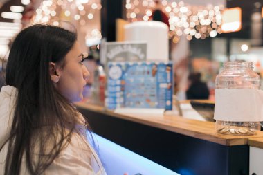 Beyaz ceketli, beyaz tenli, esmer, güzel bir kız alışveriş merkezinde tezgahın arkasında durup şekerleme alıyor. Çevrimdışı alışveriş kavramı.