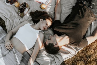 Güzel bir Kafkasyalı mutlu esmer çift piknikte sepeti ve meyveleri olan bir battaniyeye uzanıyor ve yaz günü şefkatle birbirlerinin gözlerinin içine bakıyor..