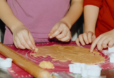 Tanımlanamayan iki beyaz kız masada duruyor ve ellerini fazla uzatarak pembe silikon bir paspasın üzerinde uzanan sarı ekmek hamurunu kesiyorlar. Adım adım talimatlar. Adım