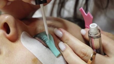 Bir genç Kafkas kozmetik uzmanı sol gözünün kirpiklerini silikon bir kalıba yapıştırıyor fırçayla yapıştırılan bir yapıştırıcıyla, kozmetoloji masasında yatan bir kadın...