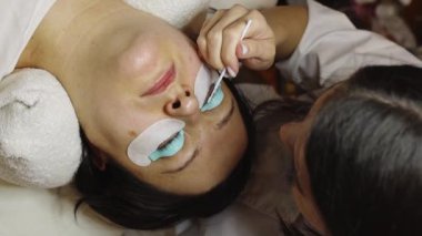 Sağ gözünün kirpiklerini silikon bir forma kaplayan beyaz, tanınmayan bir kız kozmetik uzmanı fırçayla uygulanan bir firma, kozmetik masasında yatan bir kadın.