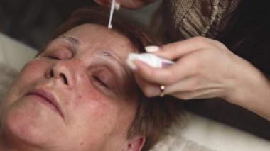 Tanımlanamayan genç bir beyaz kozmetik uzmanı tüpten bir şeyler çiziyor ve sol kaşı fırçayla güçlendiren ve iyileştiren bir kompozisyon uyguluyor.